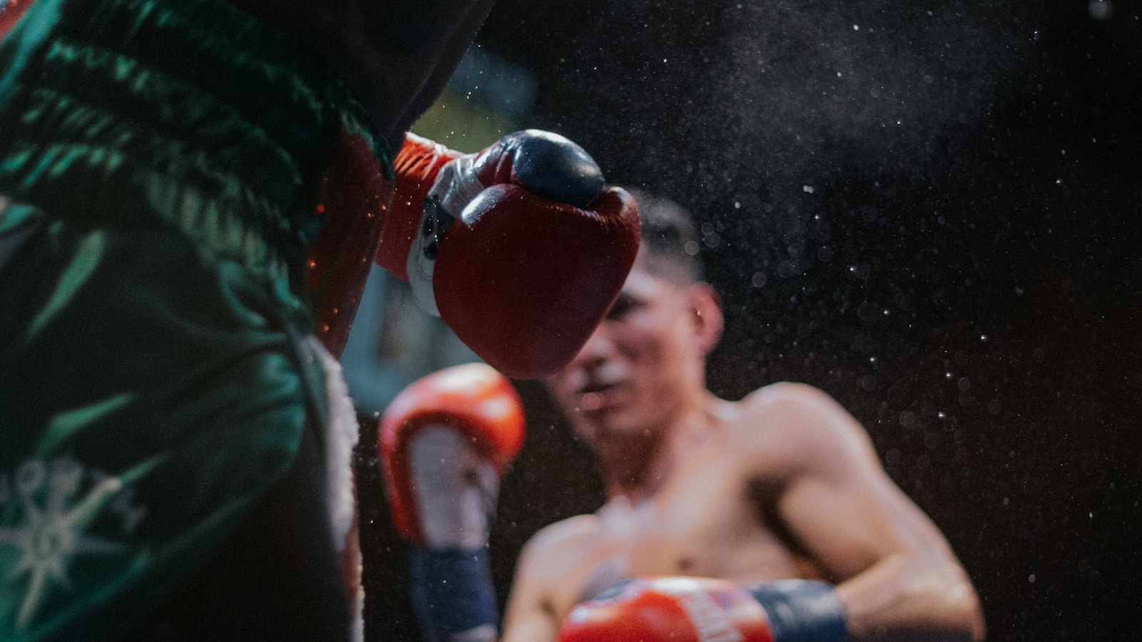 Boxer wearing red gloves striking a trainer's focus mitt in a boxing ring