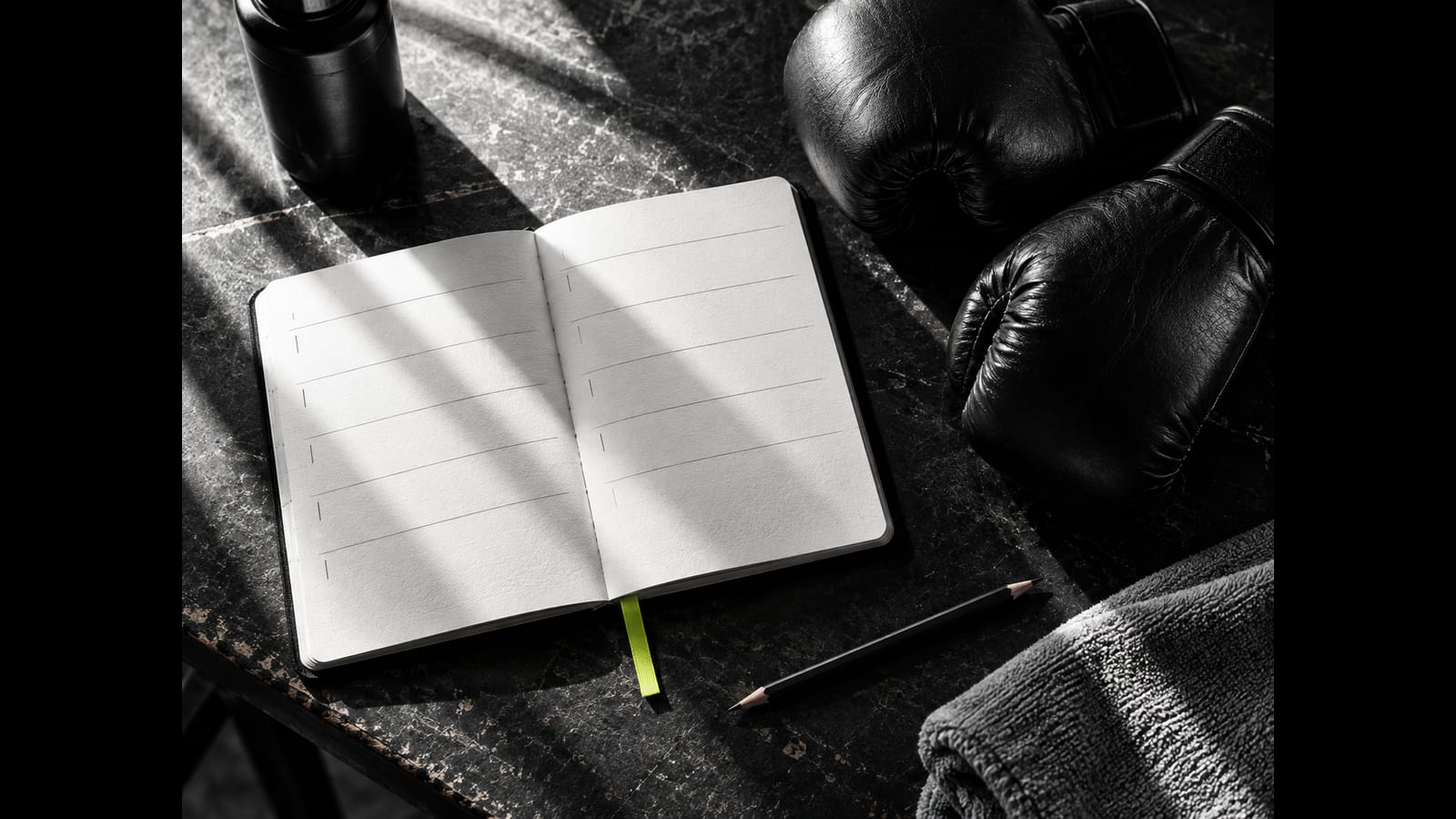 An open planner with blank rows lies beside boxing gloves, a pencil and a towel.