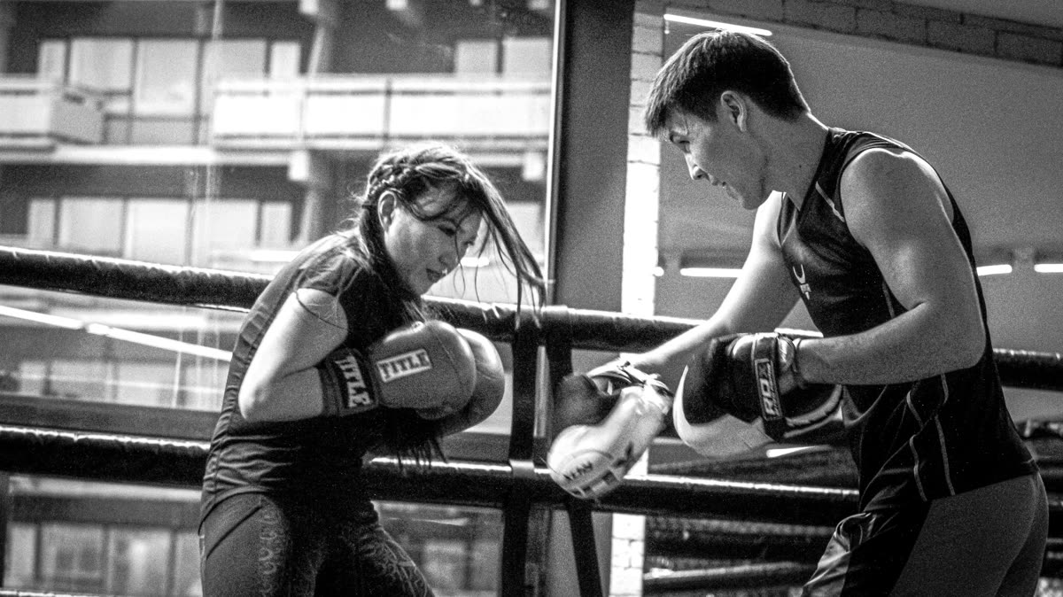 Coach demonstrating a basic boxing stance to beginners in a gym class