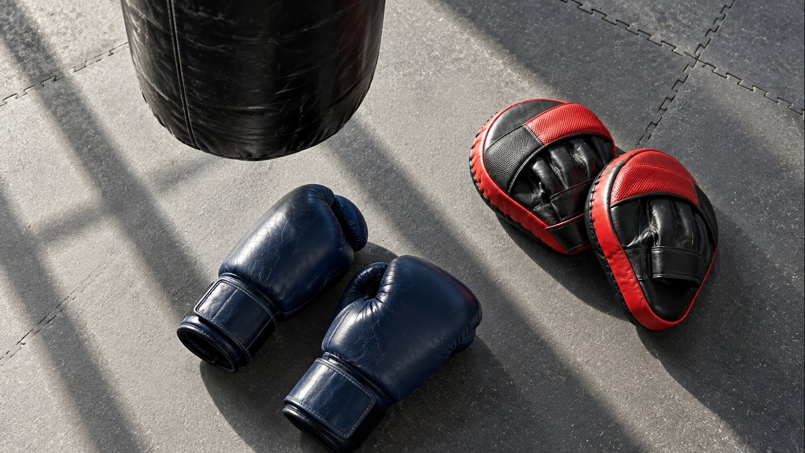 Navy boxing gloves, red focus mitts and the edge of a heavy bag on a clear training floor.